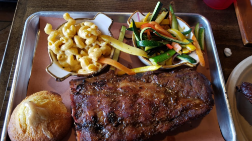 A tray with grilled ribs, macaroni and cheese, sautéed vegetables, and a cornbread muffin.