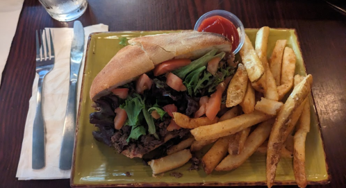 A sandwich filled with lettuce and tomatoes, served with a side of fries and a small cup of ketchup on a green plate.
