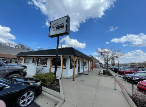 Exterior view of Snack Shack restaurant with a blue sky and clouds, surrounded by parked cars.