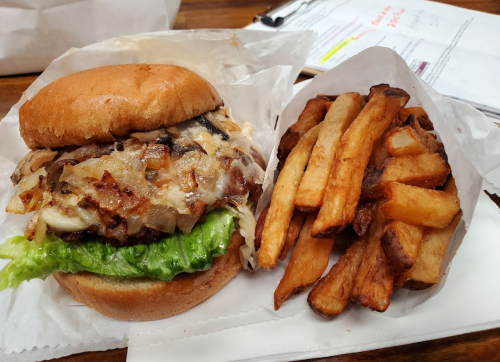 A juicy burger with lettuce, grilled onions, and melted cheese, served with a side of crispy French fries.
