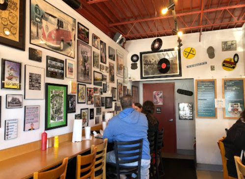 A cozy restaurant interior with a wall of framed photos, records, and vintage decor, featuring diners at a wooden table.
