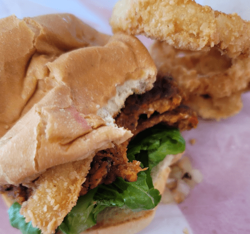 Close-up of a partially eaten sandwich with crispy chicken, lettuce, and onion rings on the side.