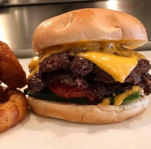 A juicy cheeseburger with melted cheese, ketchup, and lettuce, served with crispy onion rings on the side.