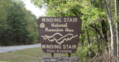 Sign for Winding Stair National Recreation Area, featuring picnic and camping information, surrounded by trees.