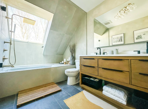 Modern bathroom featuring a bathtub, shower, wooden vanity, and large mirror with natural light from a skylight.