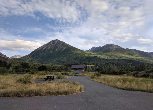Scenic view of mountains under a blue sky, with a picnic area and grassy landscape in the foreground.