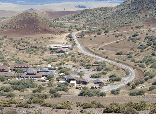A winding road leads through a dry landscape with scattered buildings and hills in the background.