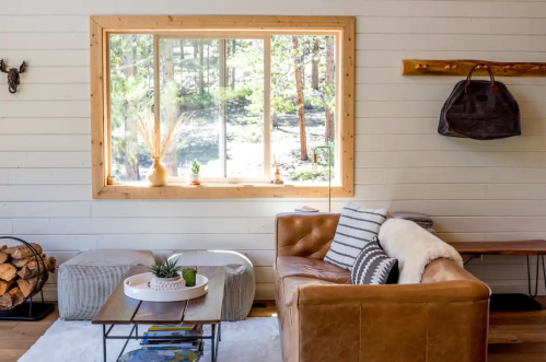 Cozy living room with a leather sofa, wooden accents, and a large window overlooking a forested area.