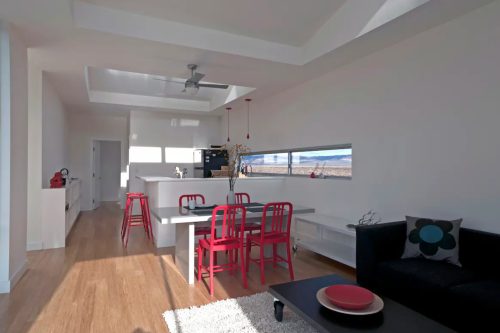 Bright, modern interior featuring a dining area with red chairs, a sleek kitchen, and large windows for natural light.