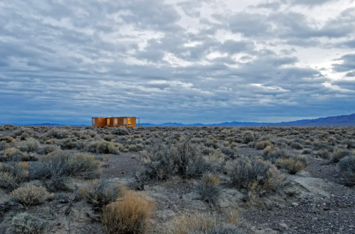 A solitary modern cabin stands in a vast, barren landscape under a cloudy sky.