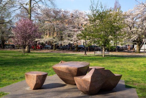 A park scene featuring abstract stone sculptures surrounded by blooming trees and green grass.