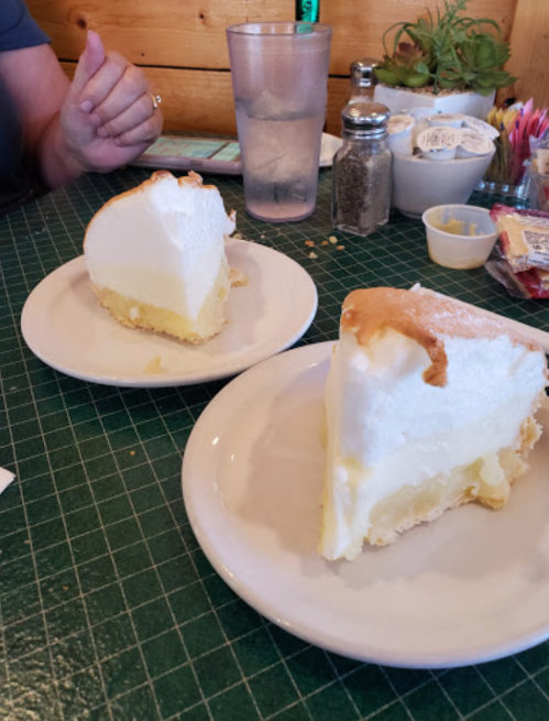Two slices of lemon meringue pie on white plates, with a glass of water and condiments in the background.