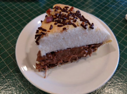 A slice of cake with a chocolate filling, topped with sprinkles, on a white plate.