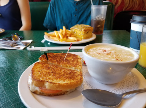 A plate with a grilled cheese sandwich, a bowl of soup, and a side of fries in a diner setting.
