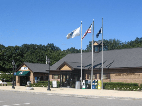 Visitor information center with flags, ATM, and parking area under a clear blue sky.