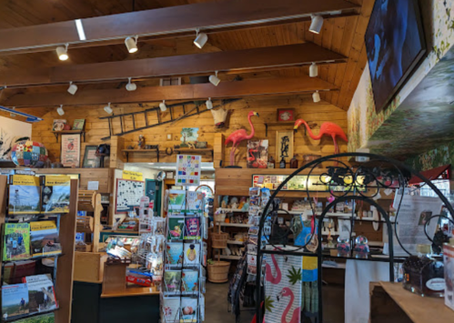 A cozy gift shop interior with wooden walls, shelves of merchandise, and decorative flamingos.