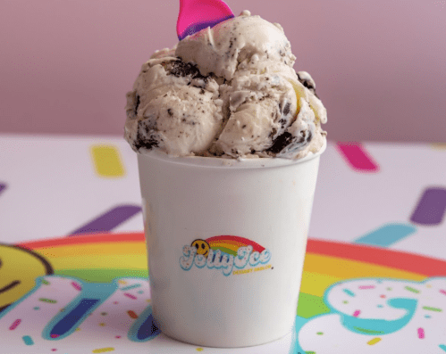 A cup of cookies and cream ice cream topped with a colorful cone, set against a playful, colorful background.