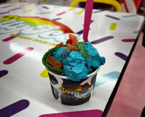 A colorful cup of blue ice cream topped with gummy candies, placed on a vibrant, patterned table.