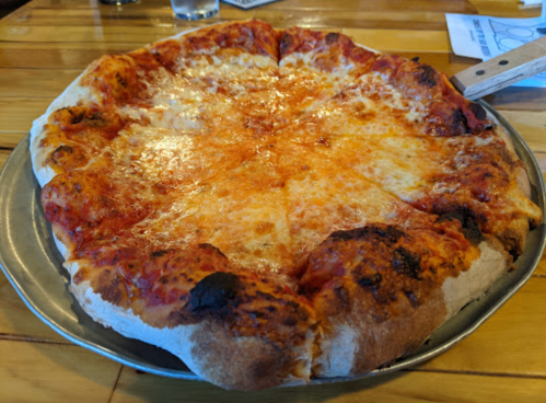 A freshly baked cheese pizza on a metal tray, with a golden crust and melted cheese, sitting on a wooden table.