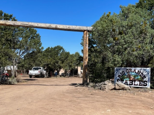 Entrance to Rio Grande Stables, featuring a wooden archway and a sign, surrounded by trees and a dirt road.