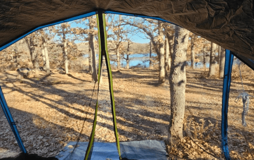 View from inside a tent, showcasing trees and a lake in the background on a sunny day.