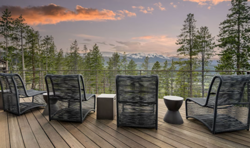 A serene deck with wicker chairs overlooking a forest and mountains at sunset.