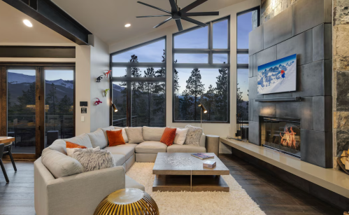 Modern living room with a large sectional sofa, fireplace, and panoramic windows showcasing a mountain view.