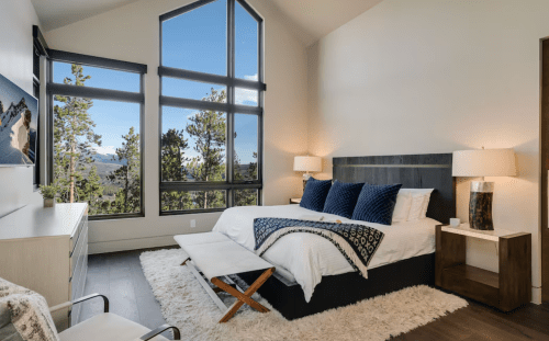 Modern bedroom with large windows, mountain views, a cozy bed, and stylish decor. Bright and inviting atmosphere.