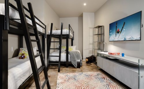 A modern bedroom with two bunk beds, a single bed, a TV, and a cozy rug on a concrete floor.