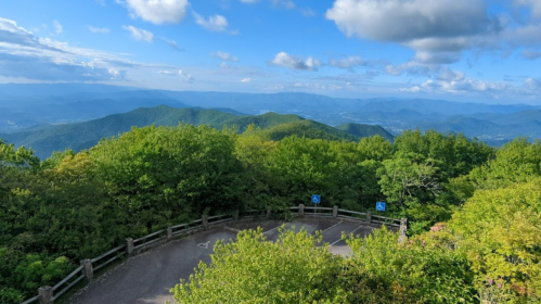 A scenic view of lush green mountains under a blue sky with clouds, featuring a winding road in the foreground.