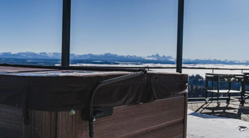 A hot tub on a deck with a stunning mountain view and clear blue sky in the background.