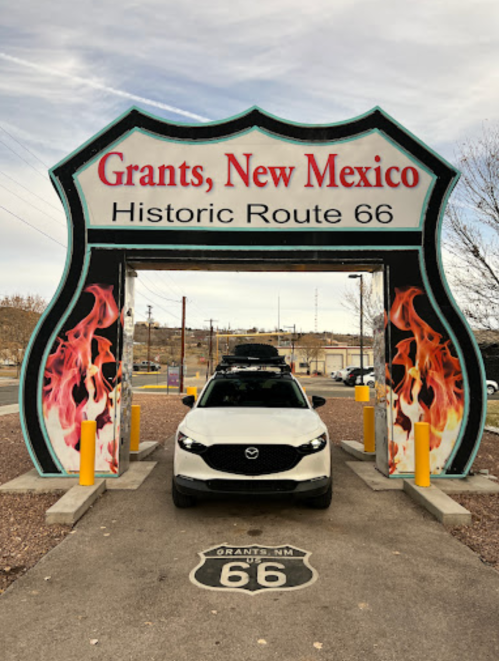 A white car parked under the "Grants, New Mexico" sign on Historic Route 66, featuring flames and a retro design.
