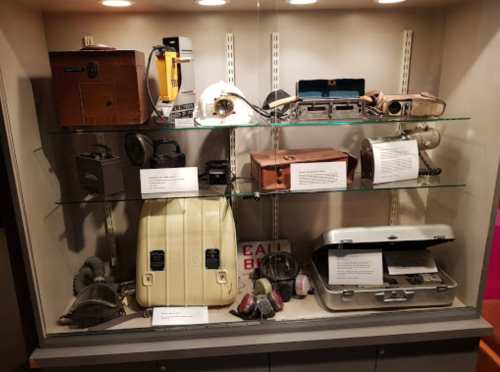 A display case featuring various vintage cameras and audio equipment on glass shelves with informational labels.