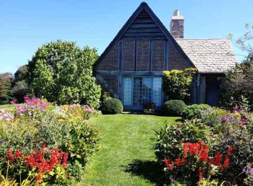 A charming house surrounded by vibrant flowers and lush greenery under a clear blue sky.