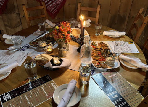 A rustic dining table set with various dishes, candles, and water glasses, surrounded by wooden chairs.