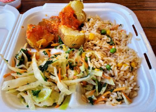 A divided takeout container with rice, a baked potato with sauce, and a side of coleslaw.