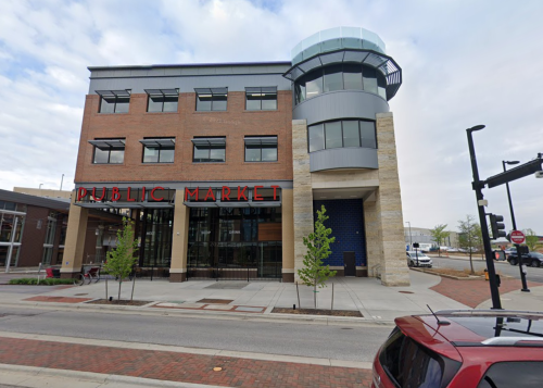A modern building with "PUBLIC MARKET" signage, featuring large windows and a unique tower, located on a city street.