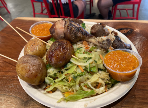 A plate of food featuring a chicken drumstick, roasted potatoes, cabbage salad, and two cups of sauce.