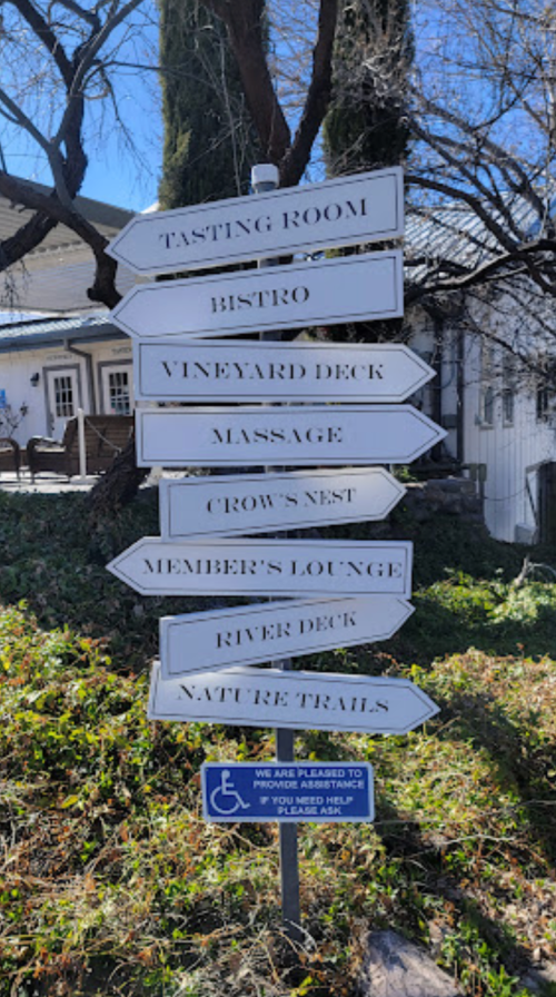 Signpost with multiple directional arrows pointing to various locations: Tasting Room, Bistro, Massage, and more.
