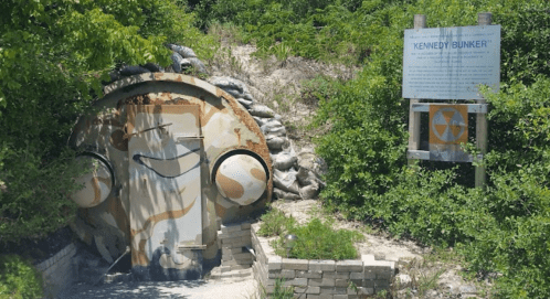 A weathered bunker entrance surrounded by greenery, with a sign labeled "Kennedy Bunker" nearby.