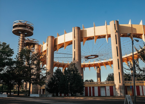 A large, circular structure with tall columns and a tower, surrounded by trees under a clear blue sky.