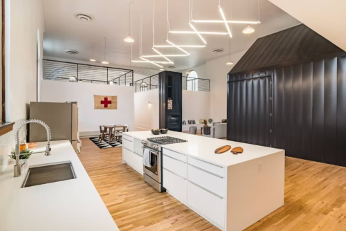 Modern kitchen with a large island, sleek appliances, and a minimalist design, featuring wooden floors and unique lighting.