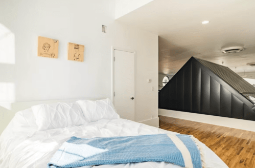 Bright bedroom with a white bed, blue blanket, and modern decor featuring two framed drawings on the wall.