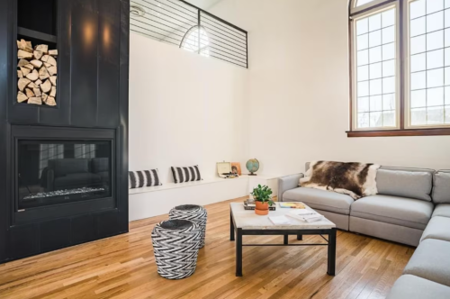 Modern living room with a gray sectional sofa, black fireplace, wooden floors, and a coffee table with decor.