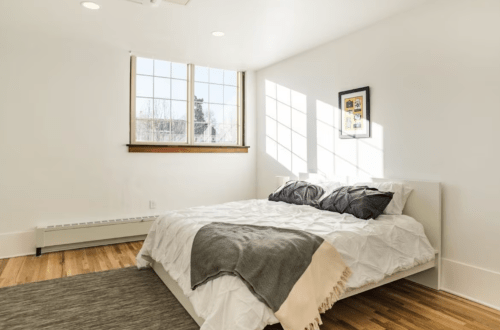 Bright, minimalist bedroom with a large bed, natural light, and a framed picture on the wall.