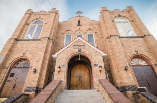 Historic brick church with a large arched entrance and cross atop, featuring tall windows and decorative details.