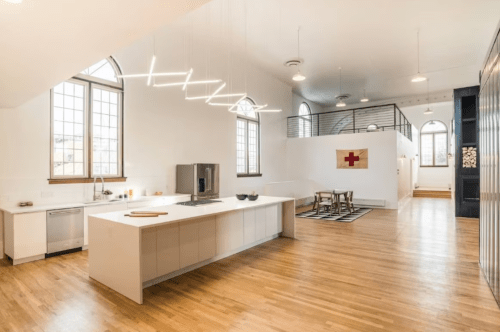 Modern kitchen with an island, large windows, and wooden floors, featuring minimalist decor and a dining area.
