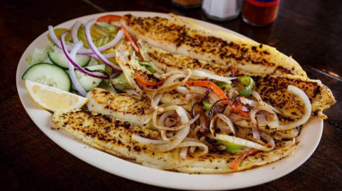 Grilled fish fillets served with sautéed onions, peppers, and fresh cucumber and onion salad on a white plate.