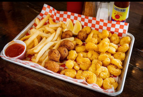 A tray of golden fried shrimp, hushpuppies, and French fries, served with a side of dipping sauce and lemon wedges.