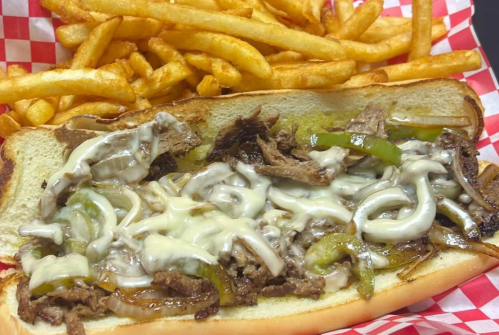 A loaded cheesesteak sandwich with sautéed onions and green peppers, served with a side of crispy French fries.